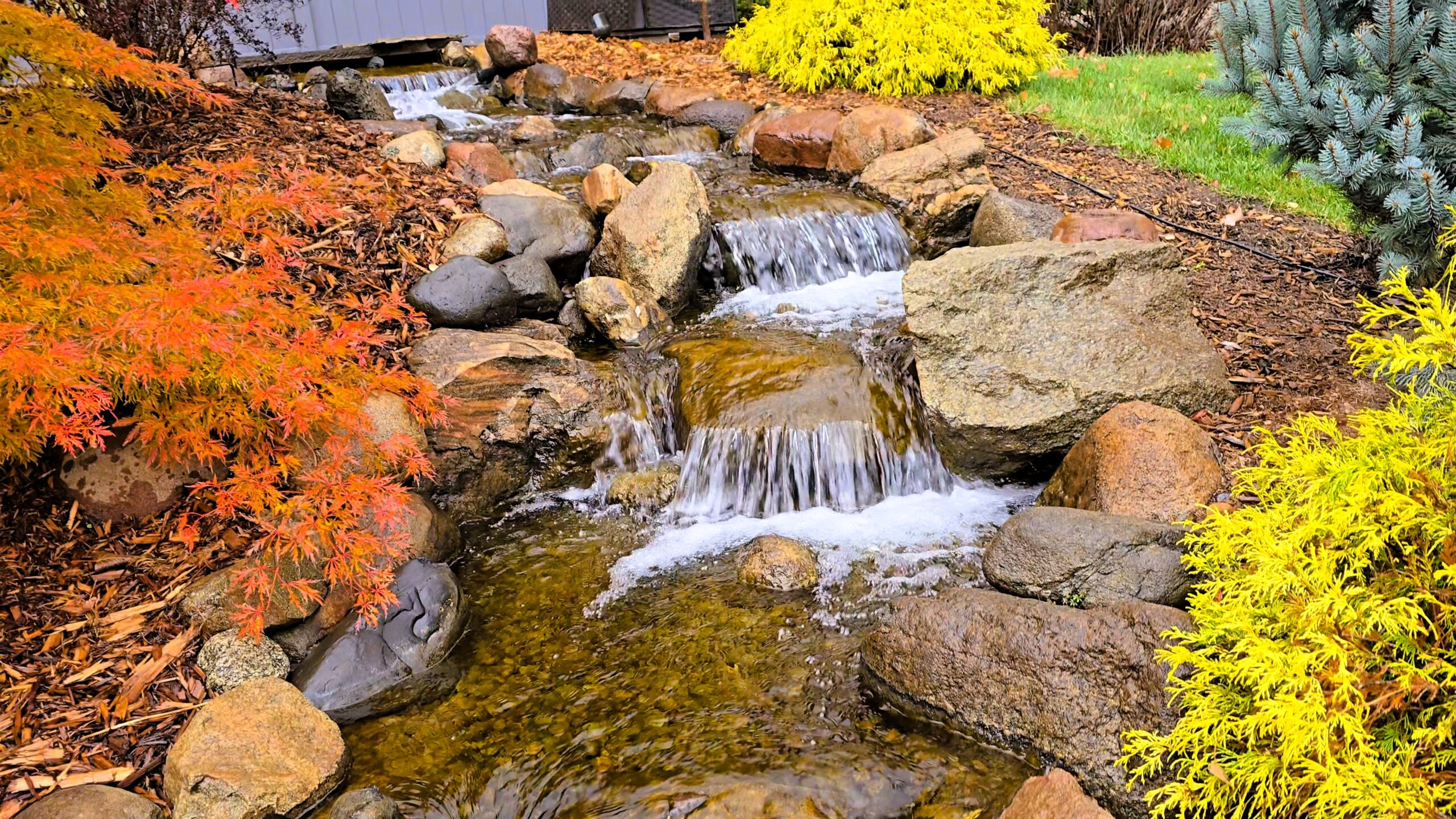 Stream and waterfall system connected to large swimming pond with intake bay filtration upgrade, designed to reduce skimmer clogging and maintenance in Orono, Minnesota
