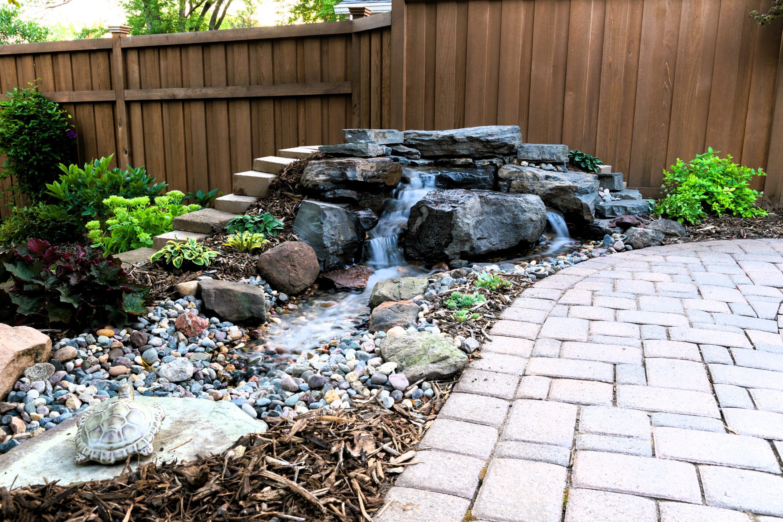 _MG_7962 Compact pondless waterfall installation in Mendota Heights, MN featuring natural Banded Jasper stone, cascading water, decorative gravel stream, and surrounding landscape plants.