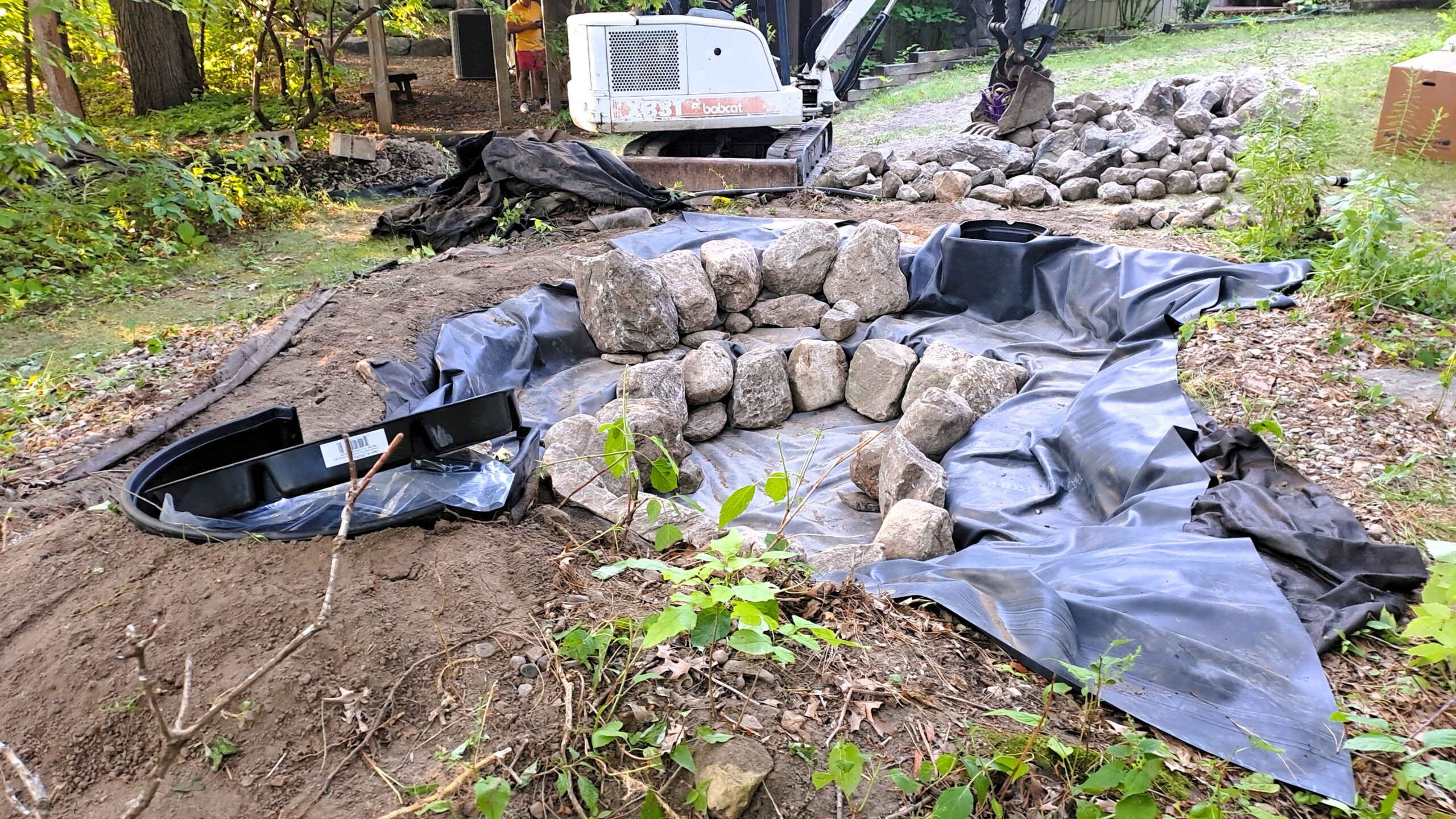 Waterfall structure assembly with natural boulders and BioFalls filter box in backyard pond construction in Minnesota