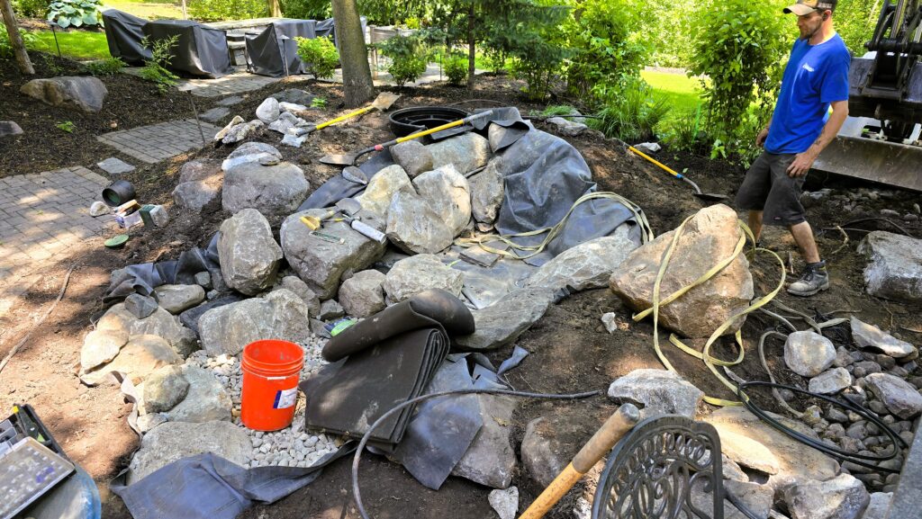 Expert placement of native Minnesotan granite boulders and river rock over the pondless waterfall liner during the final stages of water feature construction.