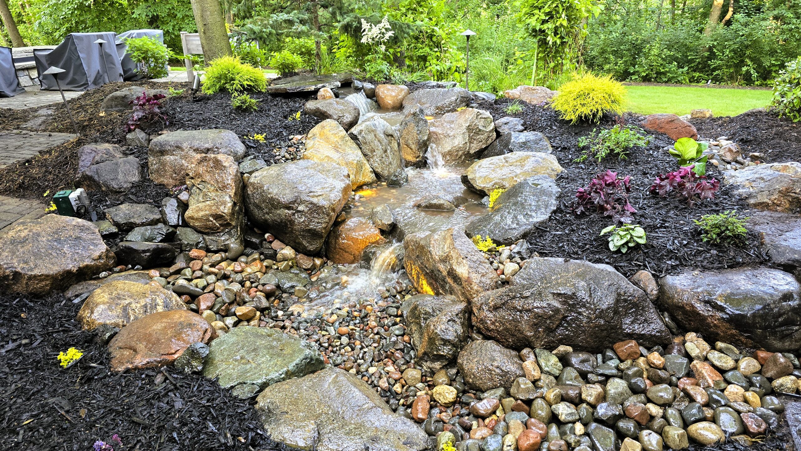 Expert placement of native Minnesotan granite boulders and river rock over the pondless waterfall liner during the final stages of water feature construction.