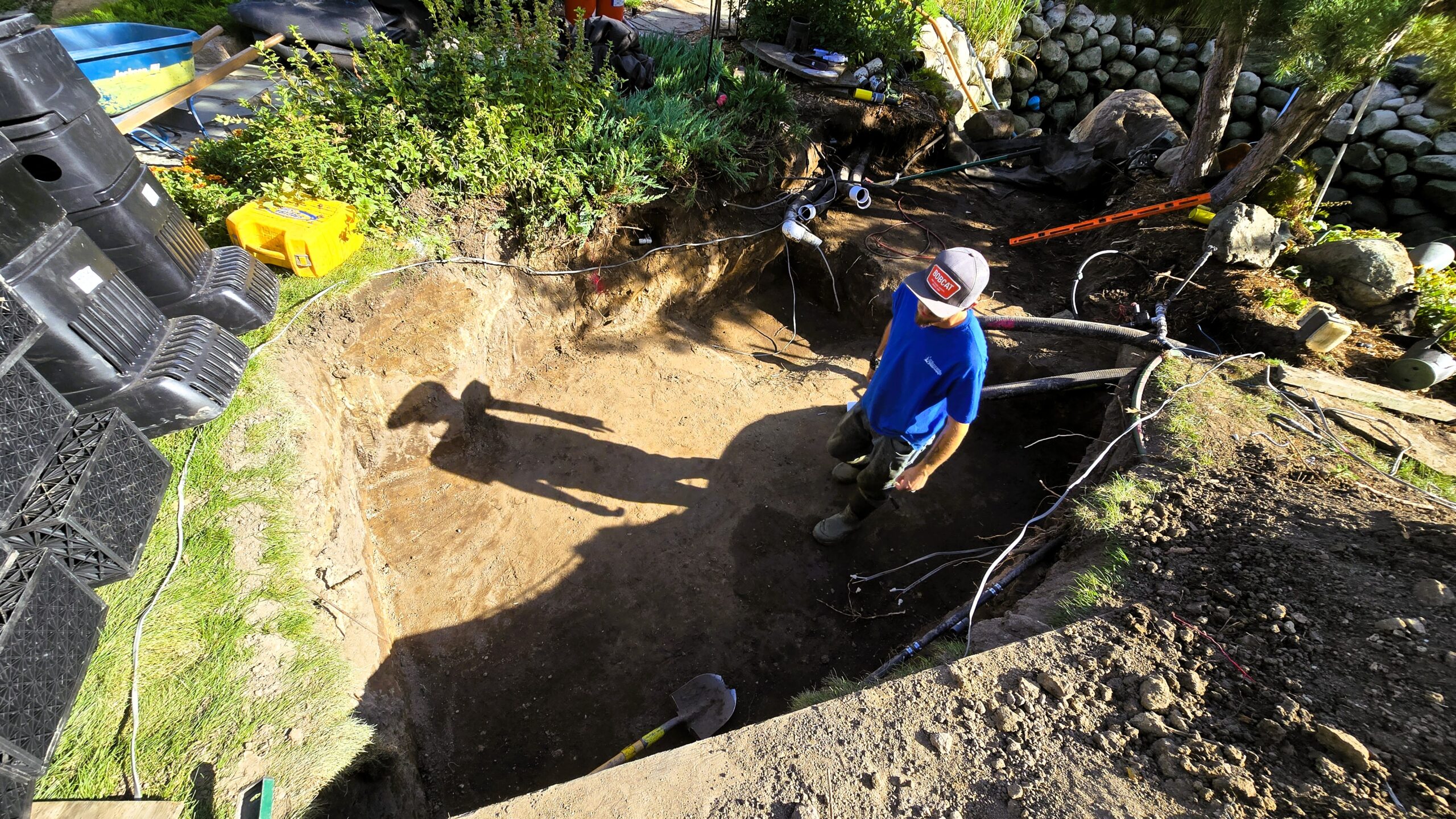 Excavation area with exposed underground utilities during intake bay installation, complicating construction of large swimming pond system in Orono, Minnesota