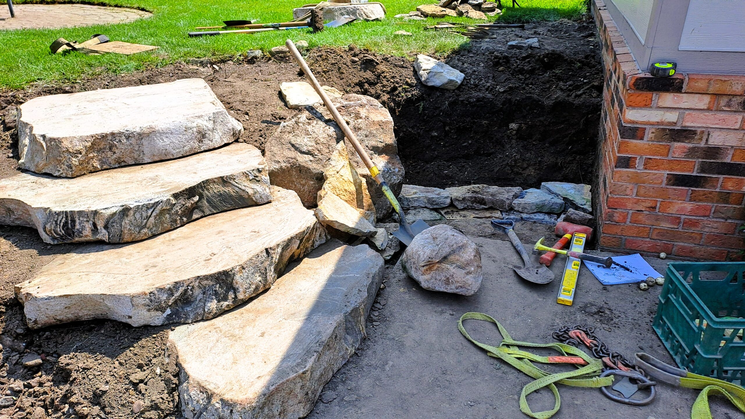 Installation of large hand-cut natural stone steps beside a backyard pond during construction in St. Michael, Minnesota