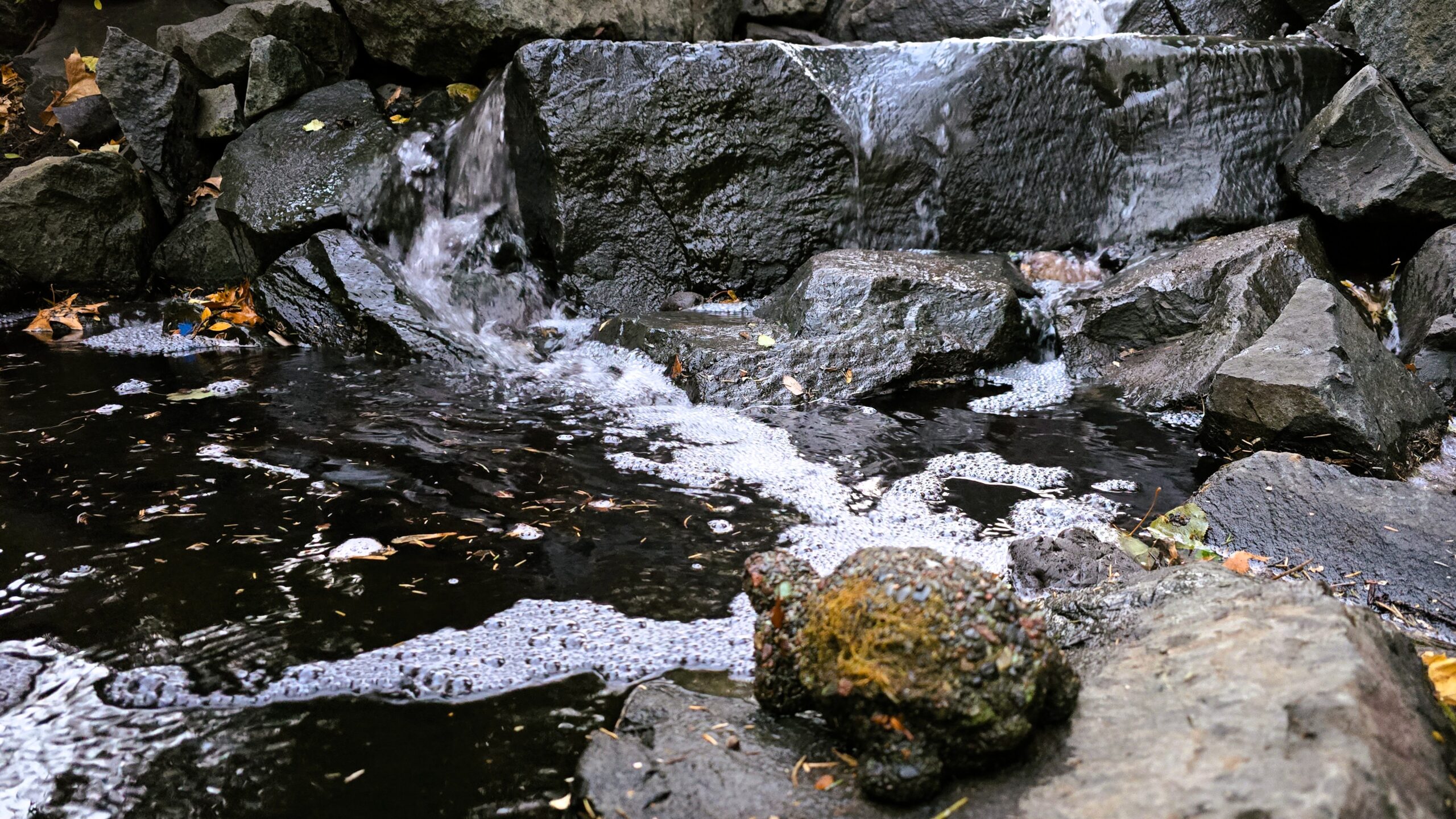 Water flowing over a wide natural trap rock waterfall after a backyard stream renovation in Arden Hills, MN.