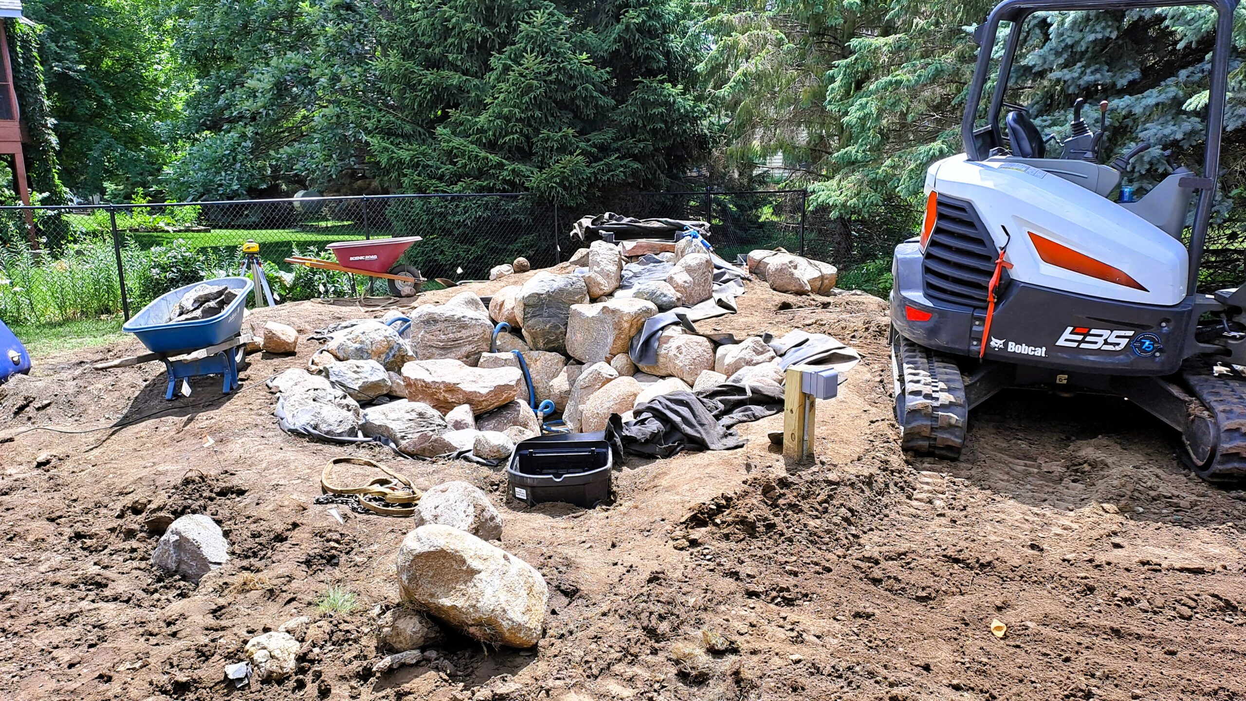 Backyard fish pond and waterfall under construction with natural boulders in Northfield, Minnesota.