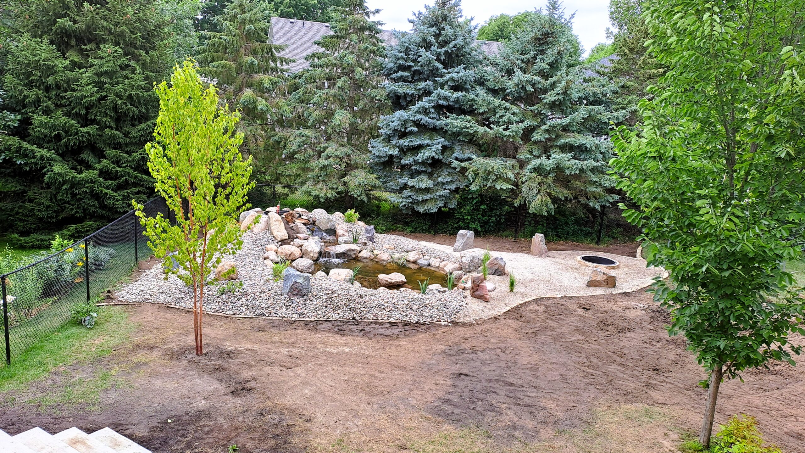 Completed backyard fish pond with waterfall, island, patio, and fire ring in Northfield, MN.
