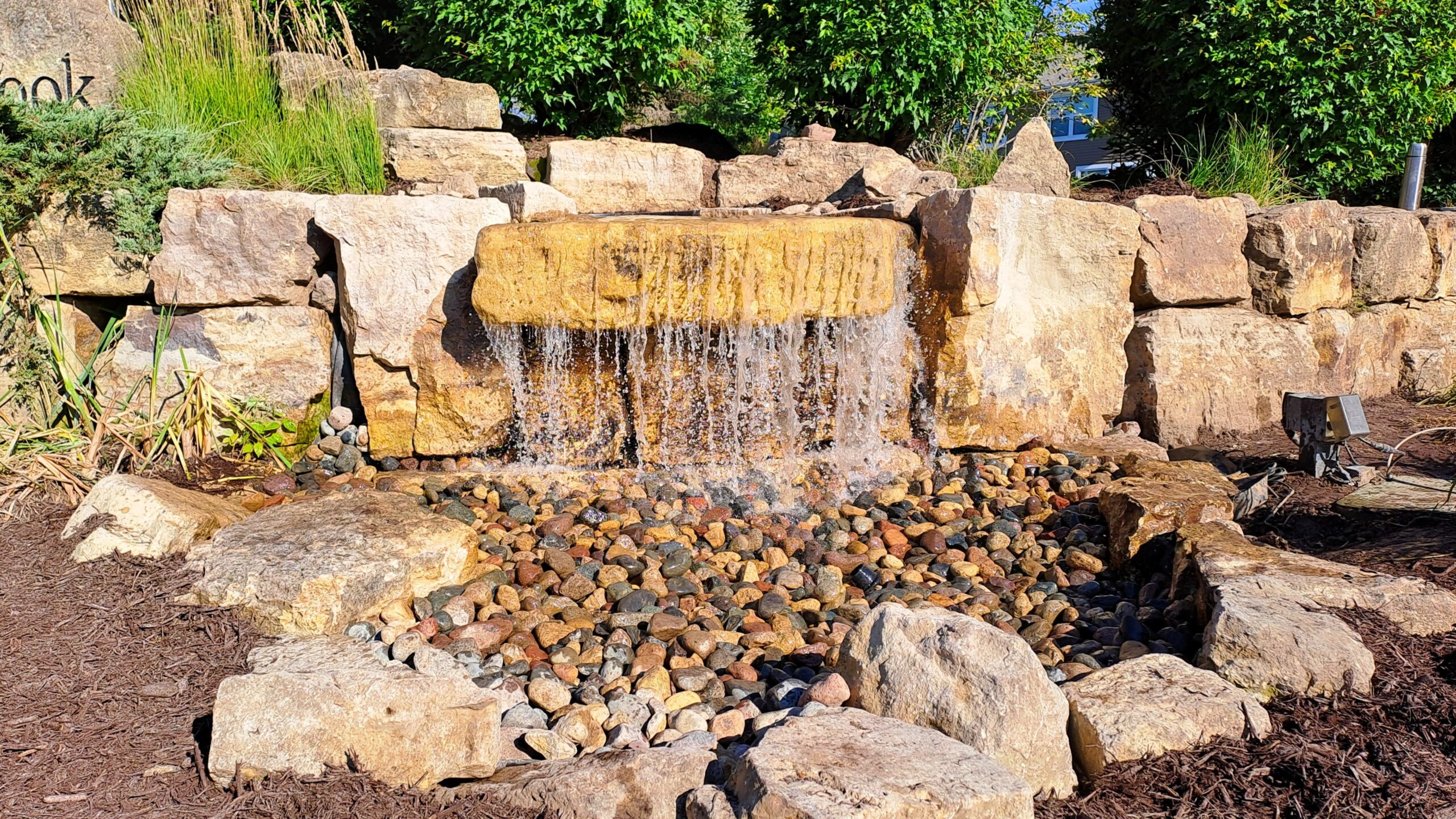 Wide limestone pondless waterfall at the Millbrook community entrance in Minnesota, featuring a high-flow cascading sheet of water over natural stone.