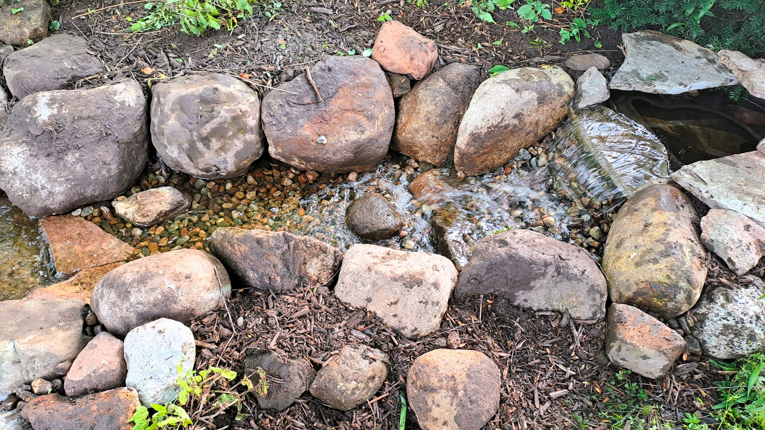 Rebuilt backyard stream in Rogers, Minnesota, with natural stone and restored waterfall flow.