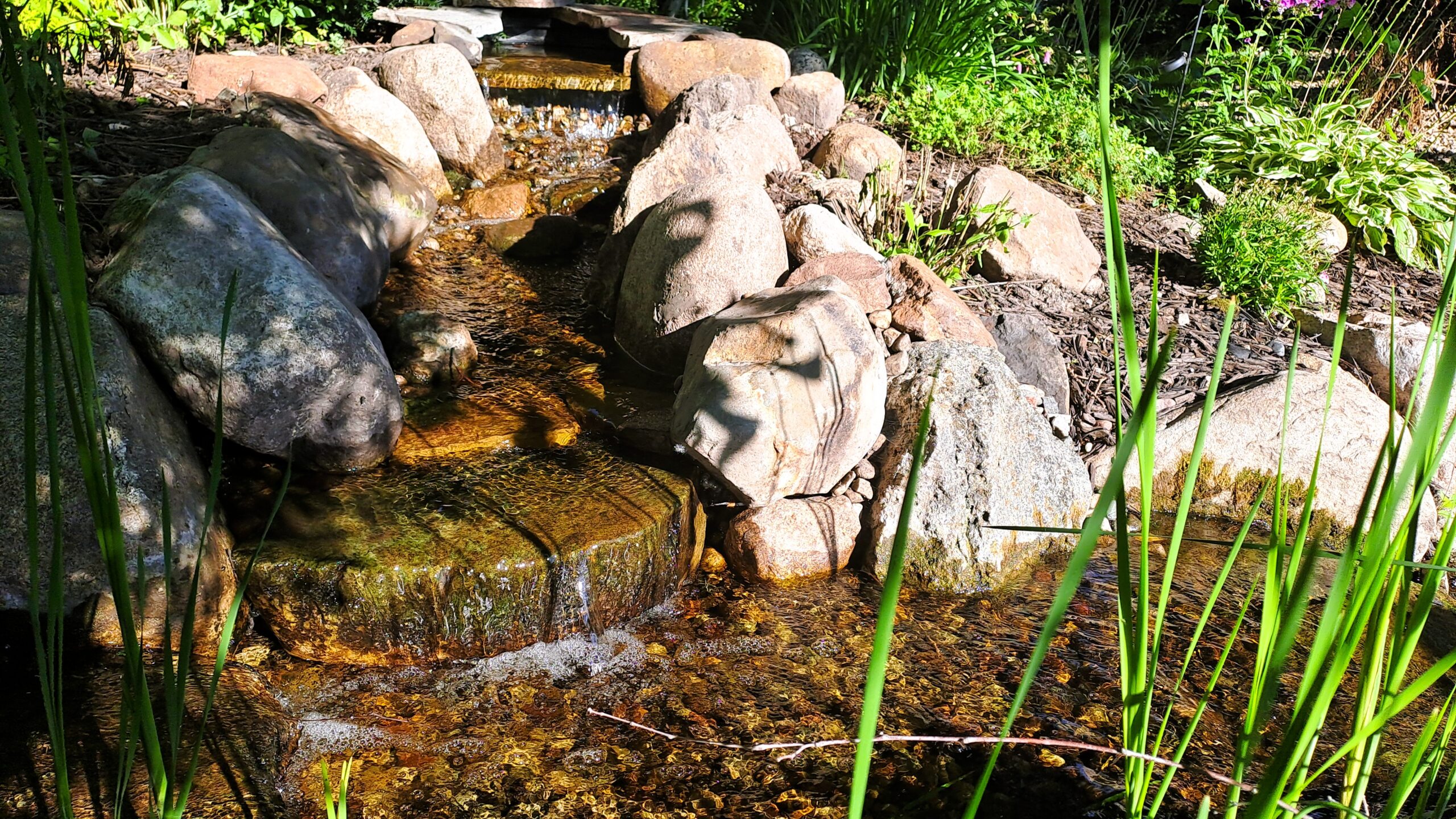 Completed backyard stream repair and 6-foot stream rebuild in Rogers, MN, with natural stone waterfalls.