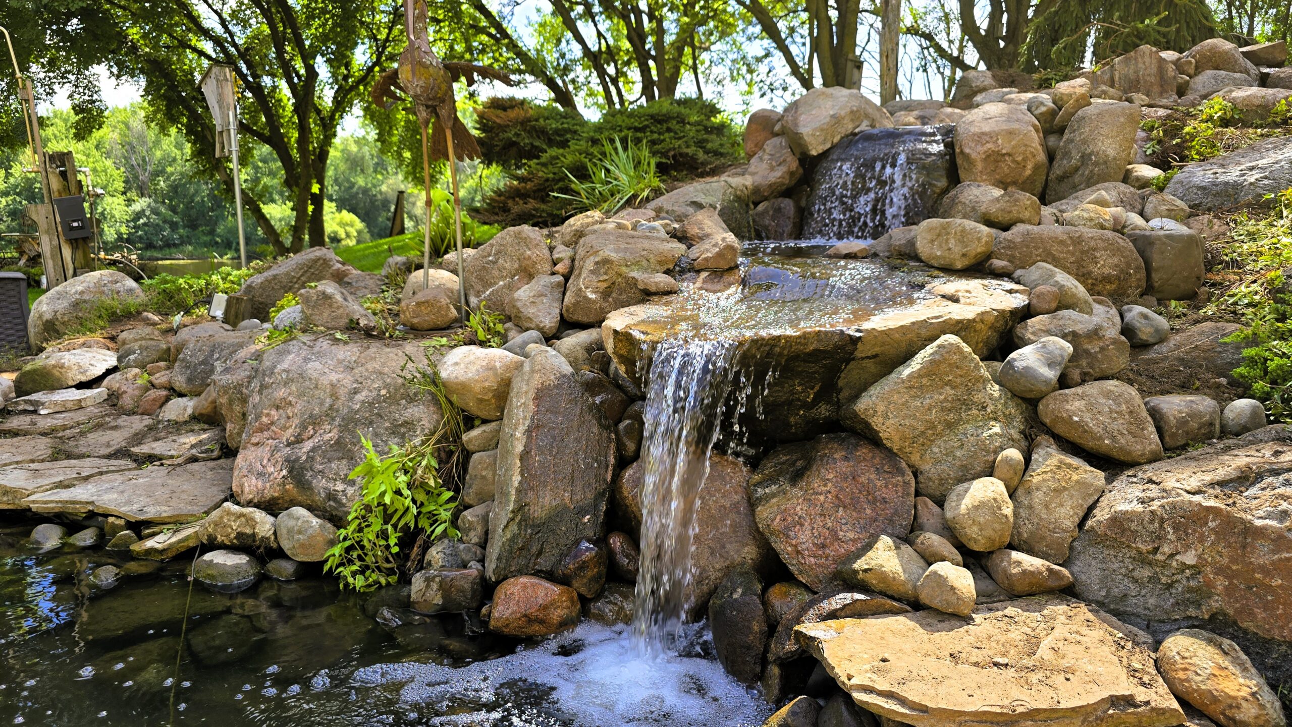 Close-up of a rebuilt backyard stream in Elk River, MN featuring natural stone waterfalls, upgraded cascades, and improved water flow.